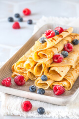Pile of rolled pancakes with rasperries and blueberries on white background