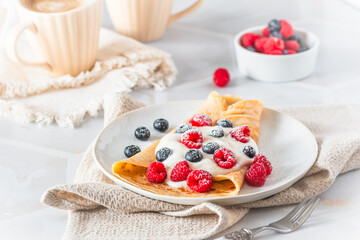 Pile of rolled pancakes with rasperries and blueberries on white background