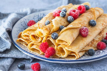 Pile of rolled pancakes with rasperries and blueberries on light blue background