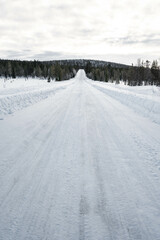 Fototapeta premium Snow covered road in North Finland on a sunny winter day. Travel Finland landscape background.