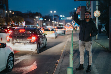 A man wearing casual attire signals for a ride amidst heavy traffic on a city street during the evening, showcasing urban life and transportation challenges.