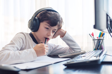 A child aged 7-9 sits at home behind a computer, writing assignments in a notebook. The image captures remote learning, digital study routines,  challenges associated with autism and ADHD. copyspace