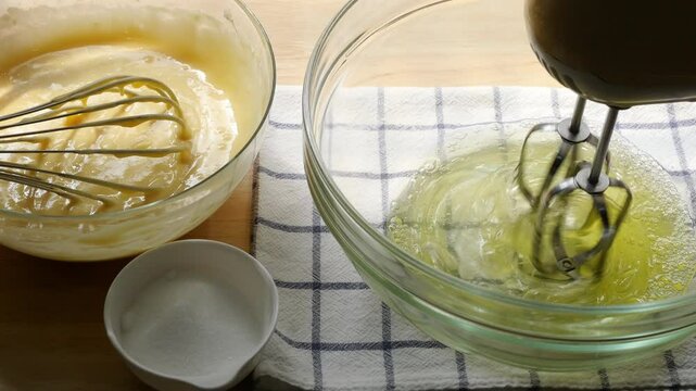 Whisking Egg Whites with Hand Mixer While Preparing Cake Batter &ndash; Baking Process with Sugar and Creamy Mixture in Glass Bowls on Kitchen Counter