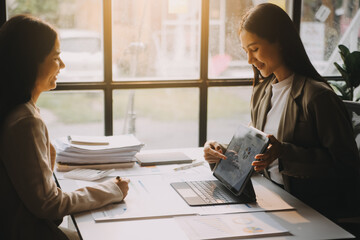 Two young Asian business woman talk, consult, discuss working with new startup project idea presentation analyze plan marketing and investment in the office.
