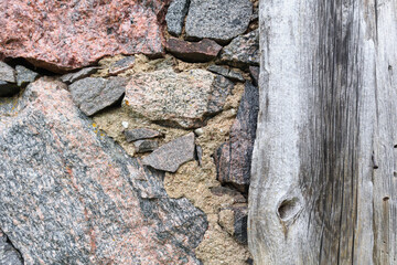 
a stone wall composed of stones of various colors and sizes, with a wooden post attached to it.