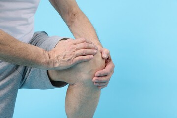 Senior man suffering from knee pain on light blue background, closeup. Space for text