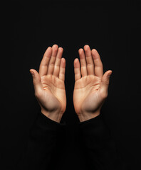 Fototapeta premium Elevated hands in mystic gesture against dark background, showcasing slim fingers and serene expression. image evokes sense of calm and introspection