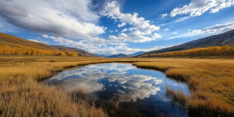 Obraz premium Autumn landscape with vibrant foliage reflecting in a tranquil lake under a blue sky with fluffy clouds