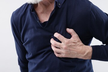 Heart attack. Senior man suffering from pain in chest on light background, closeup