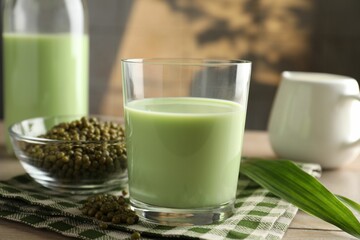 Fresh mung bean juice in glass, milk, leaves and seeds on wooden table, closeup
