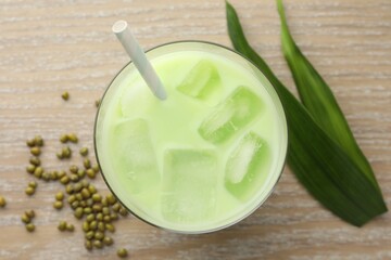Fresh mung bean juice with ice in glass, leaves and seeds on wooden table, flat lay