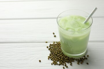 Fresh mung bean juice with ice in glass and seeds on white wooden table, closeup. Space for text