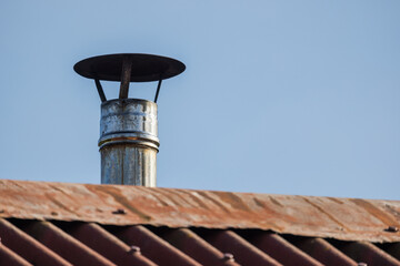 Metal chimney pipe with a protective cover on a corrugated roof