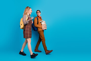 Fototapeta premium Young students cheerful and stylish walking and carrying books on blue background