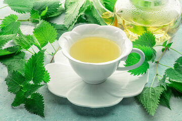 Nettle tea. Medicinal herbal tea with Urtica leaves. Fresh wild herb, in an elegant white cup with a teapot in the background