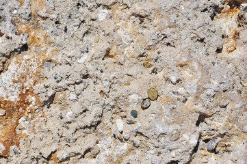 Textured surface of a weathered rocky formation in earthy tones. The close-up reveals intricate details of natural cracks, embedded minerals, and rough textures, perfect for geological backgrounds.