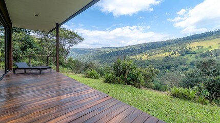 Fototapeta premium Wooden deck of a modern villa with a lounge chair overlooking a lush green valley under a blue sky.