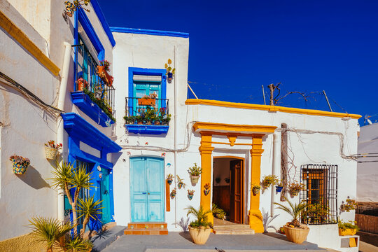 Fototapeta whitewashed facades with coloured windows and doors in a village street decorated with pots and plants. Nijar. Almeria