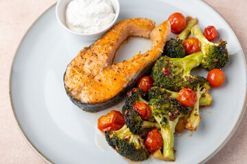 Fried salmon steak (trout) with baked broccoli and cherry tomatoes. Served with sour cream sauce with dill. Traditional home cooking. Selective focus, close-up.