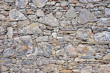 Close-up of an ancient stone wall made of irregularly shaped rocks, showcasing rustic texture and earthy tones. A perfect background representing history, architecture, and traditional craftsmanship.
