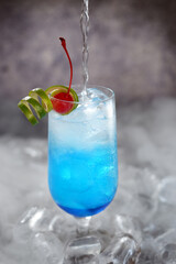 A captivating blue-hued cocktail, elegantly presented against the backdrop of a serene beach setting. This enticing drink, with its refreshing blend of tropical flavors and hint of ocean breeze, evoke