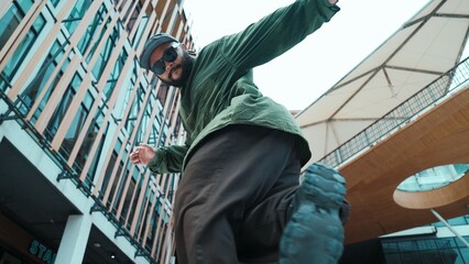 Low angle view of hipster pose in hip hop style surrounded by mall view. Portrait of sporty asian hip hop choreographer dancing break dance while looking at camera. Outdoor sport 2024. Hiphop.