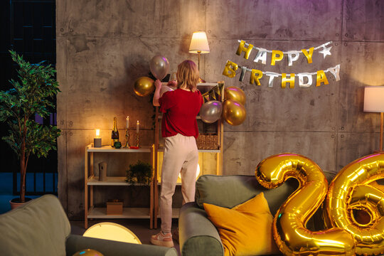 Woman decorating for 26th birthday party with balloons and happy birthday banner