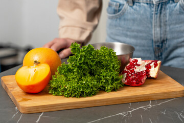 Fresh ingredients on a wooden cutting board showcasing pomegranate, lettuce, and persimmon in a modern kitchen setting