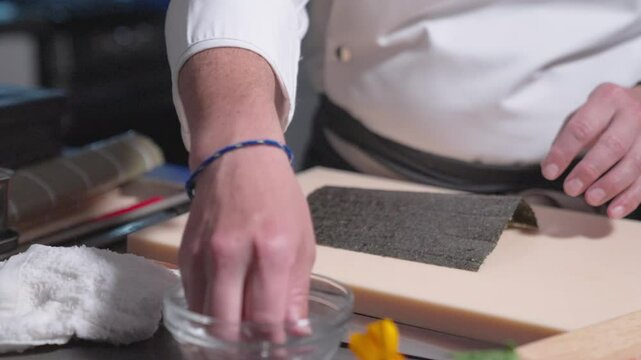 A roaming shot captures a sushi chef beginning the sushi-making process, showcasing the initial steps and technique involved. Ideal for culinary, sushi preparation, and professional kitchen content.