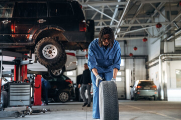 Naklejka premium Brand new tire. Male mechanic is with car in garage