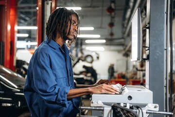 Stationary computer with display. Male mechanic is with car in garage