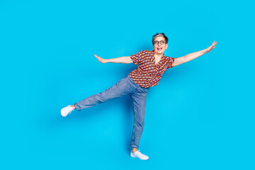 Stylish mature woman in casual attire joyfully posing against a vibrant blue background in a playful and dynamic stance.