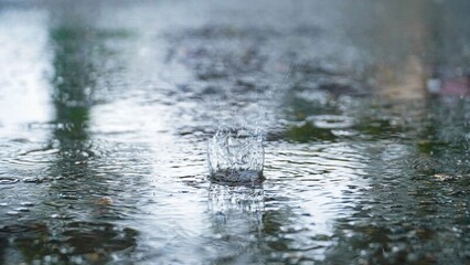 Fototapeta premium Drops of rain that fall on the asphalt when it rains. close-up rain drops. Drops of heavy rain in a puddle on the asphalt road. A Stream of water that floods all around. Rain drop splash.