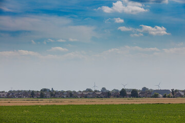 Fototapeta premium Expansive farmland under a cloudy sky with wind turbines in the distance near a small village