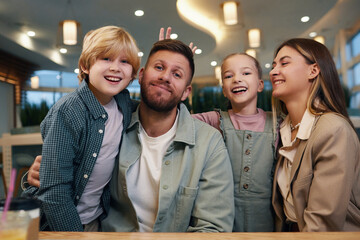 Medium shot of happy and beaming family at food court table posing for portrait while kids fooling around