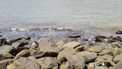 Plastic waste and debris polluting rocky shoreline, highlighting marine environmental crisis impact