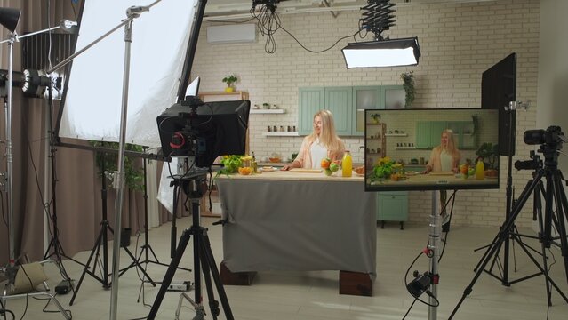 Woman host in the kitchen at the table preparing breakfast, talking and smiling, backstage video recording of a tv program in the professional studio.