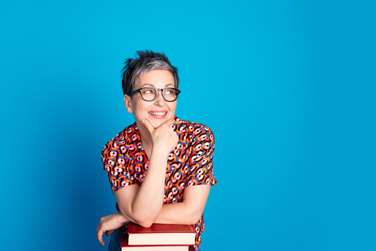 Stylish mature woman in glasses smiling with a thoughtful pose against a vibrant blue background - Powered by Adobe