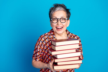 Elderly Woman Smiling with a Stack of Books, Vibrant Outfit and Blue Background