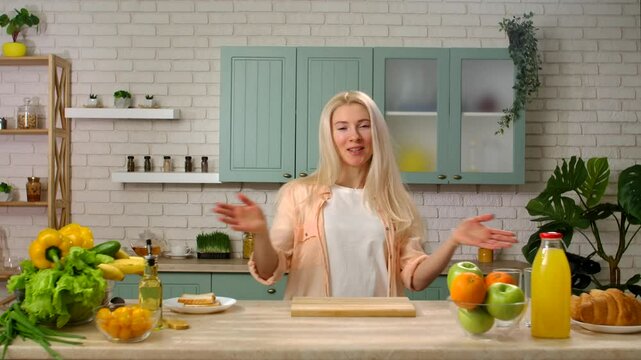 Woman host in the kitchen at the table preparing breakfast, talking and smiling, video recording of a tv program in the professional studio. Slow motion.