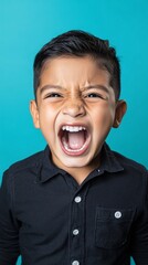 Energetic young boy wearing black button-up shirt expressing pure joy and excitement with wide open mouth and squinted eyes against vibrant turquoise studio background.