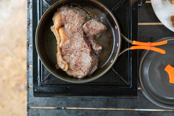 Grilled meat on hot pan for making steak or barbecue during camping. man is grilling meat on a pan over a picnic gas stove after going camping to increase the convenience of grilling meat and speed.