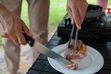 Grilled meat on hot pan for making steak or barbecue during camping. man is grilling meat on a pan over a picnic gas stove after going camping to increase the convenience of grilling meat and speed.