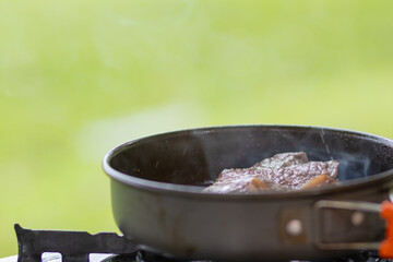 Grilled meat on hot pan for making steak or barbecue during camping. man is grilling meat on a pan over a picnic gas stove after going camping to increase the convenience of grilling meat and speed.