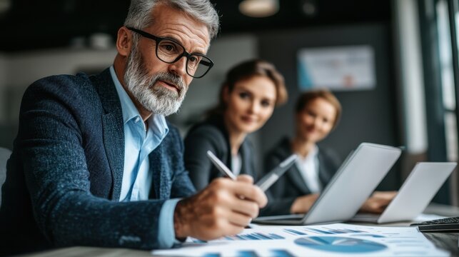 Senior couple reviewing financial portfolio together in modern office environment with documents and electronic devices - Powered by Adobe