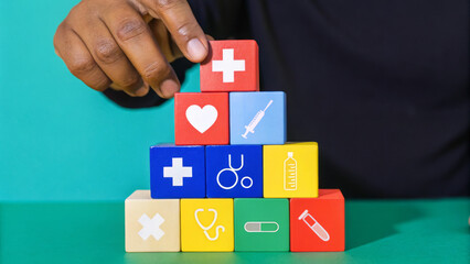 Obraz premium Hand adding cube with medical symbol to stack of cubes with health icons