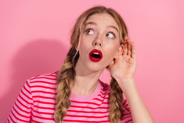 Young woman with blonde braids listening attentively on pink background, wearing stylish striped...