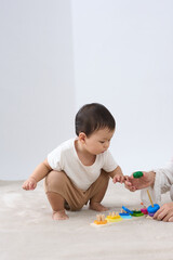 .The image features a baby sitting on the floor and playing with toys. The baby is holding onto an adult's hand while engaging in playtime. 