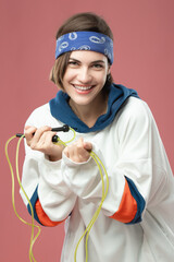 Beautiful young girl in a hood with a skipping rope in hands on a pink background