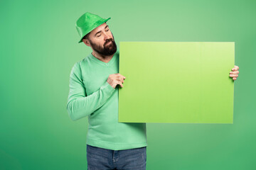 Bearded man with green St. Patrick's Day hat showing blank placard on green background